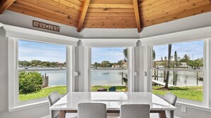A dining area with a large table and four chairs, large windows with a view of a lake and surrounding landscape.