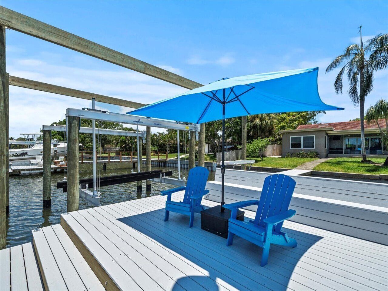 Une terrasse en bois avec deux chaises Adirondack bleues et un parasol bleu.