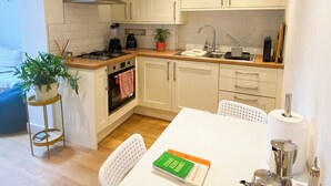 Una cocina moderna con armarios blancos, una estufa y un lavamanos. Hay una mesa de comedor con sillas y un libro encima.