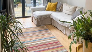 Una sala de estar moderna con un ventanal grande, un sofá con cojines estampados, un tapete a rayas de colores y una planta en maceta.