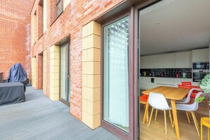 Eine Außenpatio mit Tisch und Stühlen, ein überdachter Grill und eine Glastür zum modernen Küchenbereich.