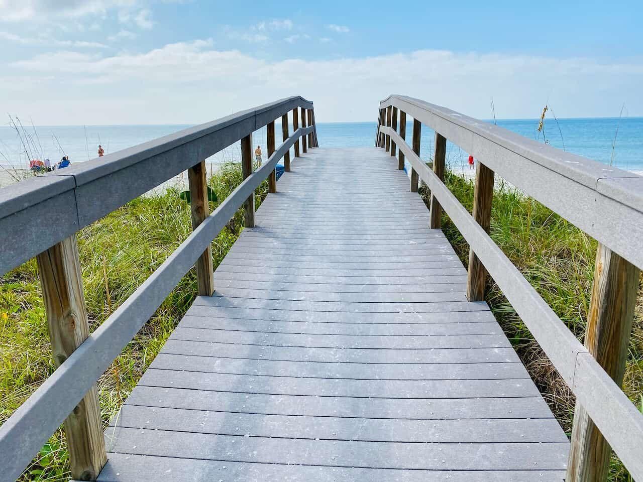 Una passerella di legno conduce a una spiaggia con vista libera sull'oceano.