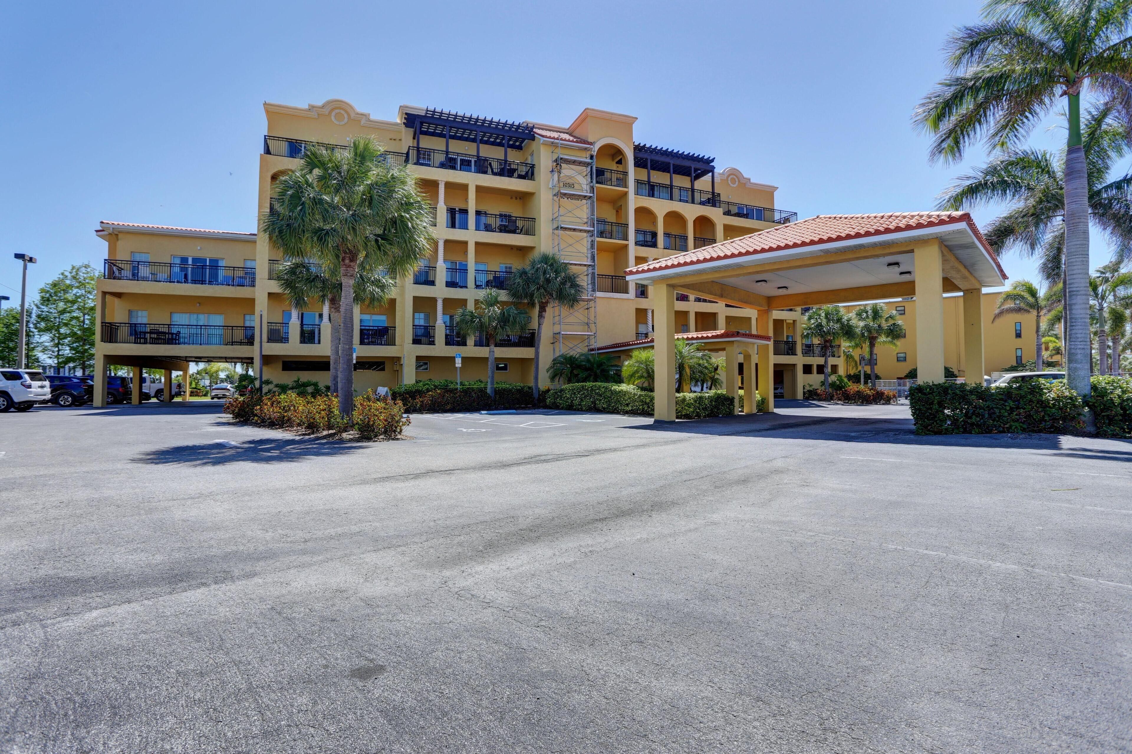 A multi-story hotel with a yellow facade, balconies, and a covered parking area.