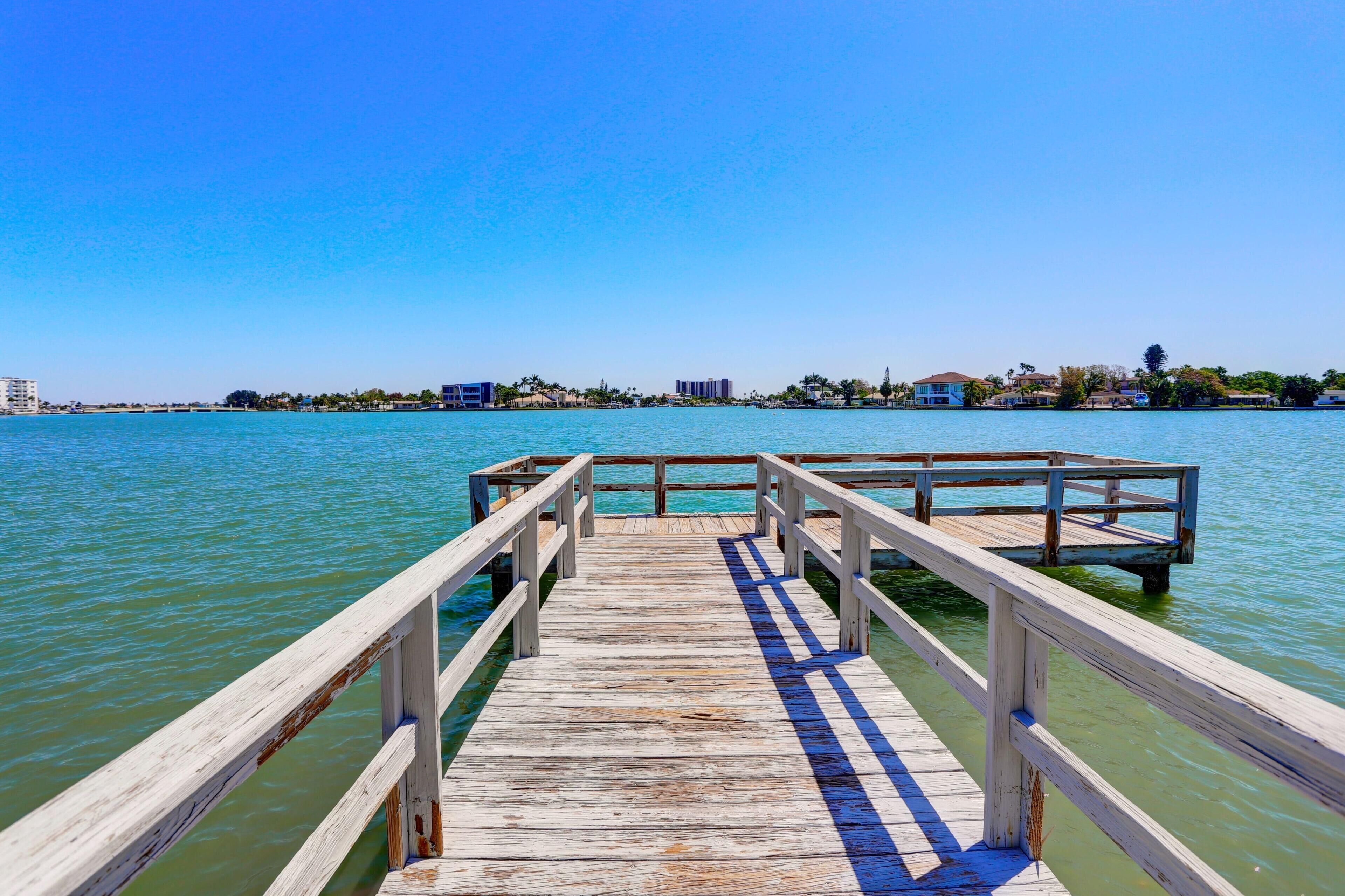 A wooden pier extending into a body of water with buildings in the background.