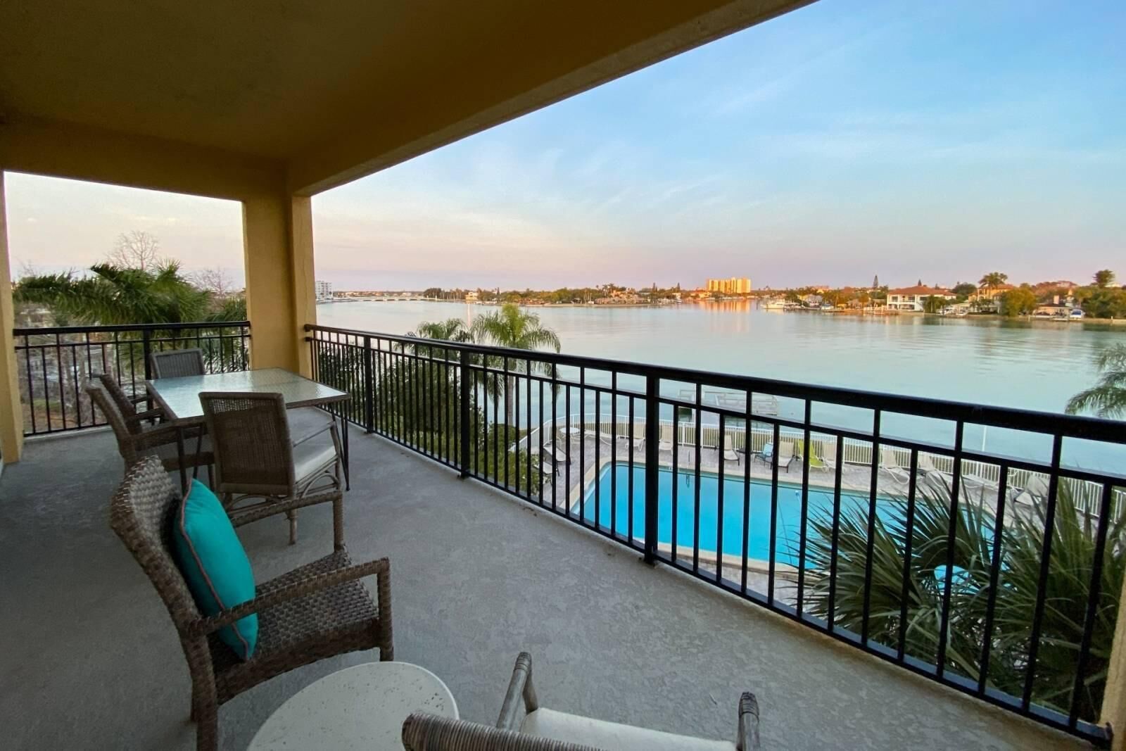 A balcony with a view of a lake, a pool, and a dining area with chairs and a table.