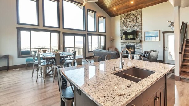 A spacious kitchen with a granite countertop, a built-in sink, and a stone fireplace. There are large windows providing natural light and a view of the outdoors.