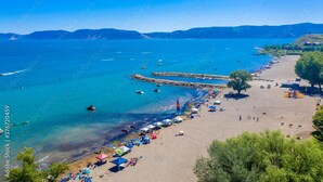 A coastal beach with clear blue waters, a rocky breakwater, and beach umbrellas.