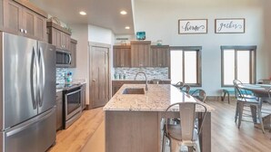 A modern kitchen with a central island, stainless steel appliances, wooden cabinets, and a dining area with a table and chairs.