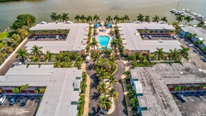 Eine Vogelperspektive auf ein Hotel mit einem zentral gelegenen Pool, umgeben von Palmen und einer Uferpromenade.