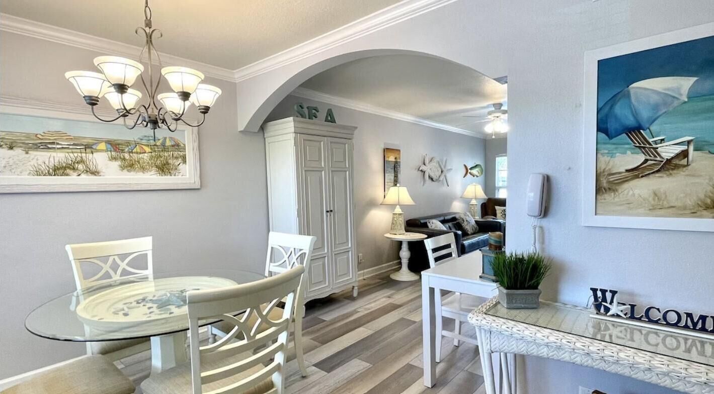 A dining area with a glass table, white chairs, a chandelier, and a 'Welcome' sign.