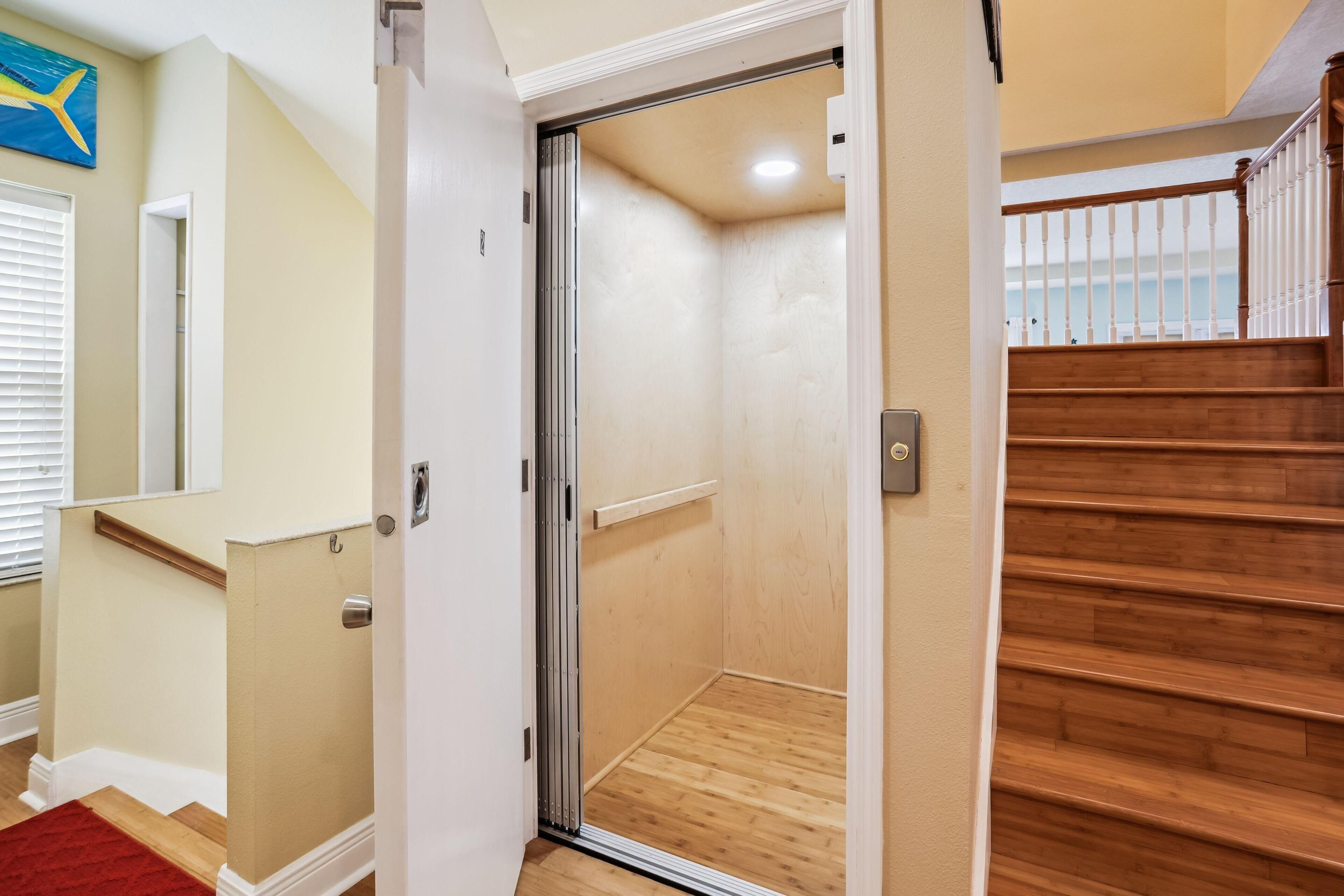 A room with a wooden floor, a white door, and a view of a wooden staircase.
