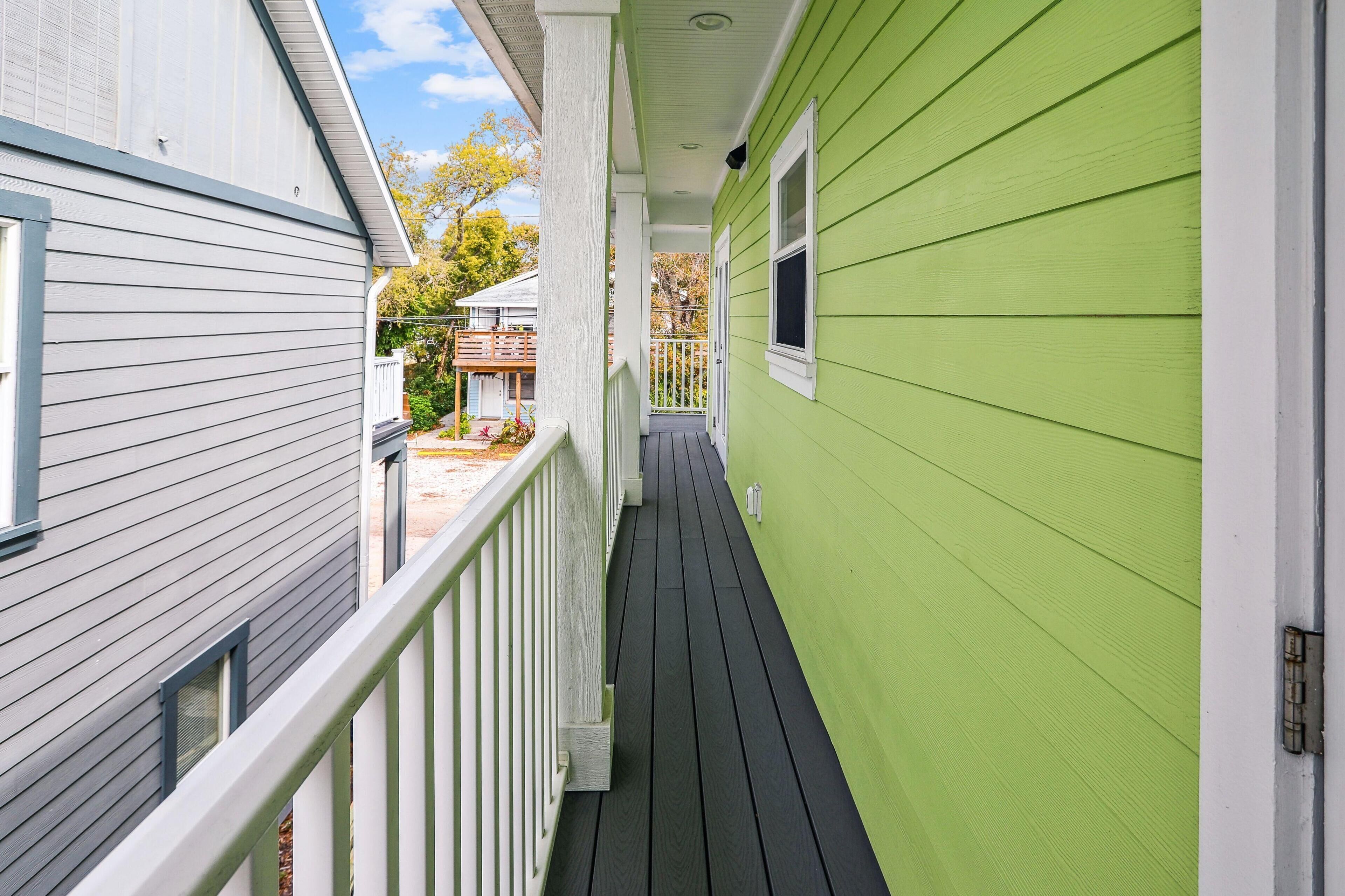 A narrow wooden deck with white railings, connecting two houses with green siding and white trim.