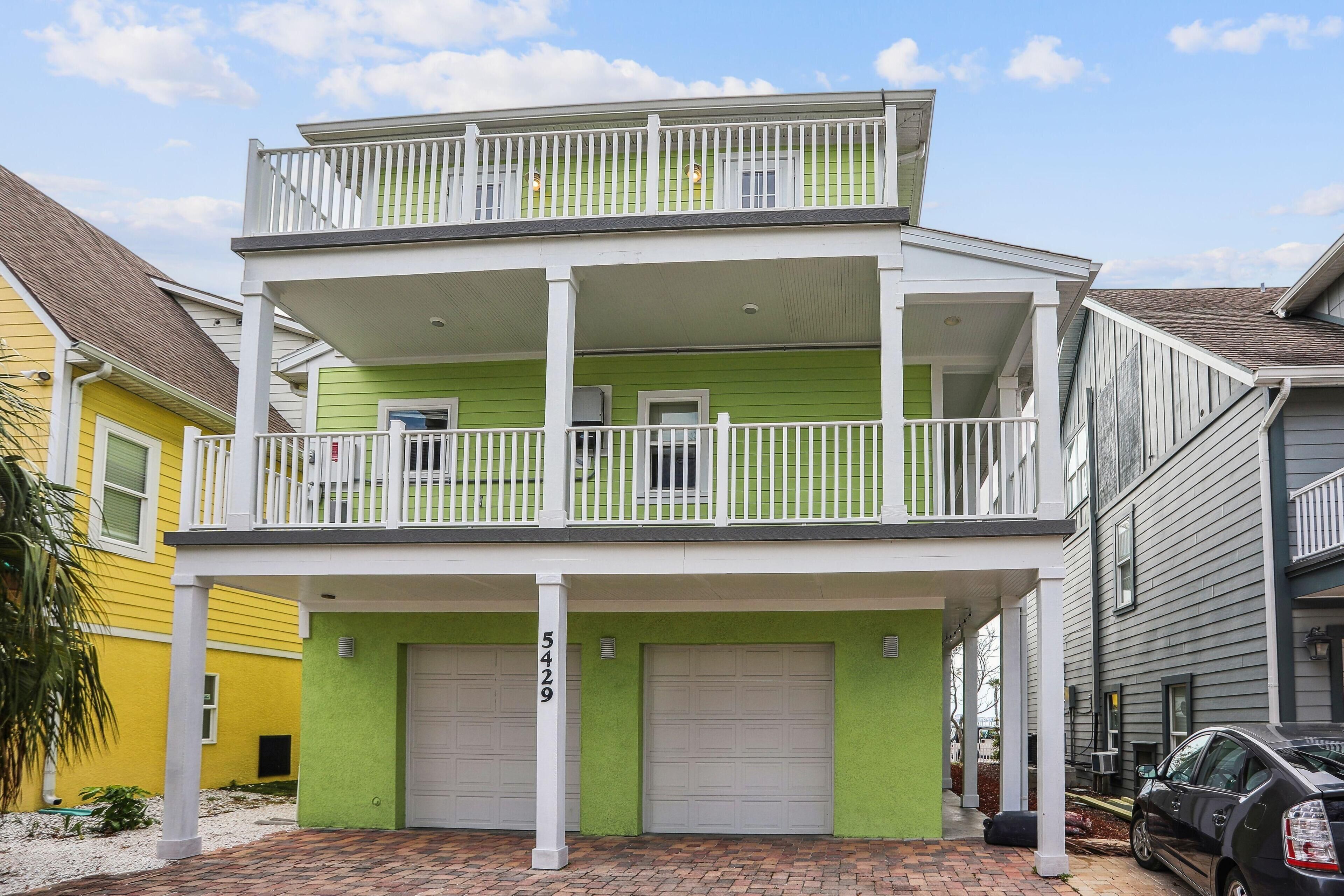 A two-story building with a balcony, two garage doors, and a brick driveway.