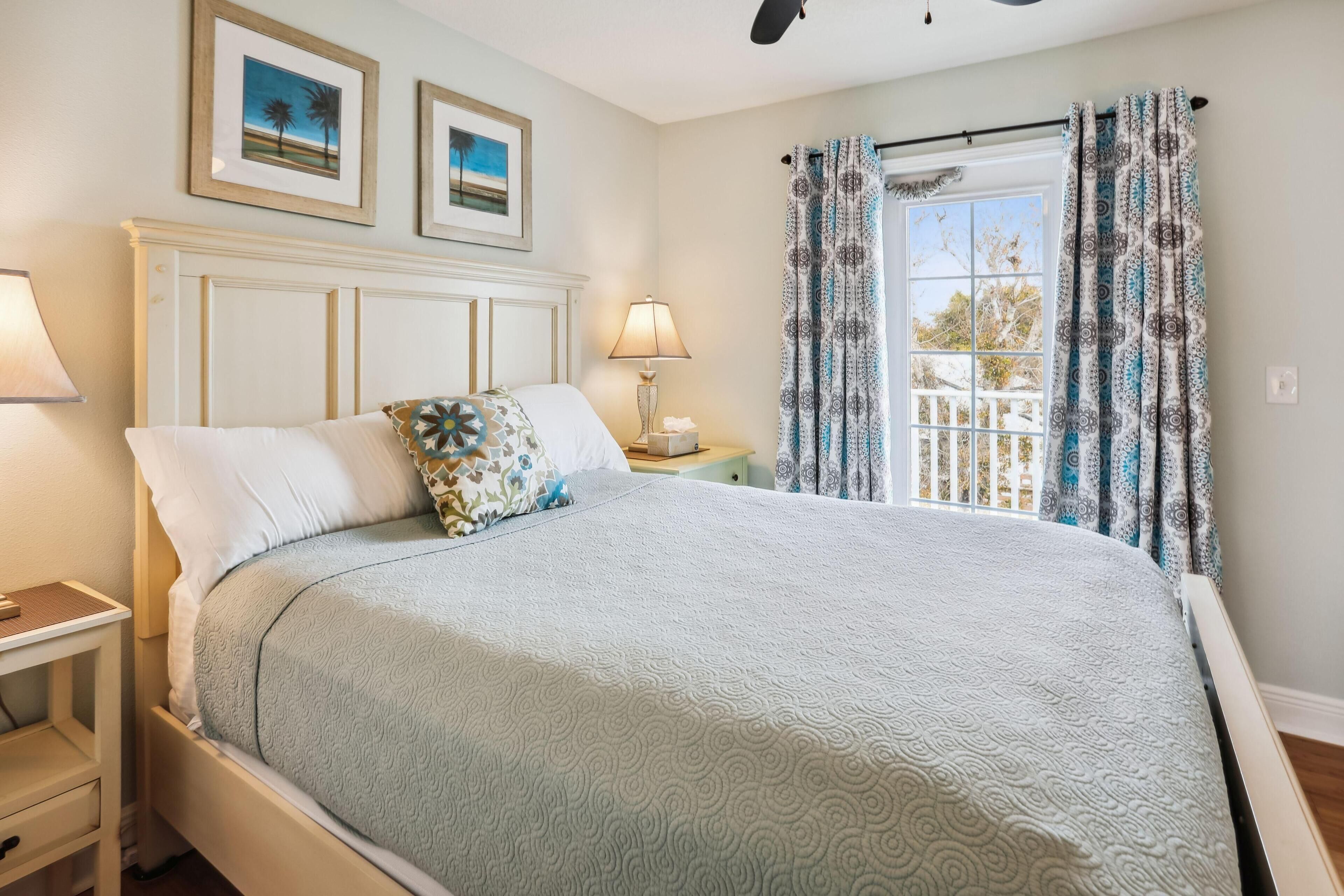 A neatly made bed with a patterned bedspread, a bedside table with a lamp, and a window with patterned curtains.