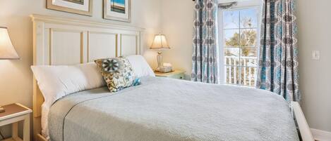 A neatly made bed with a patterned bedspread, a bedside table with a lamp, and a window with patterned curtains.