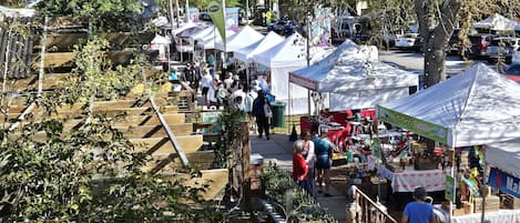 An outdoor market with various stalls and tents, surrounded by trees and a wooden fence.