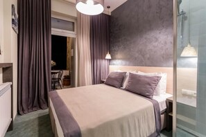 A modern hotel room with a large bed, a bedside table, a window with curtains, and a view of the outside. - Spacious 3BR • 2 Baths • Steps from Freedom Square (T'bilisi)