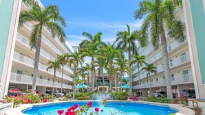 Un hôtel doté d’une piscine centrale, entourée de palmiers et de balcons.