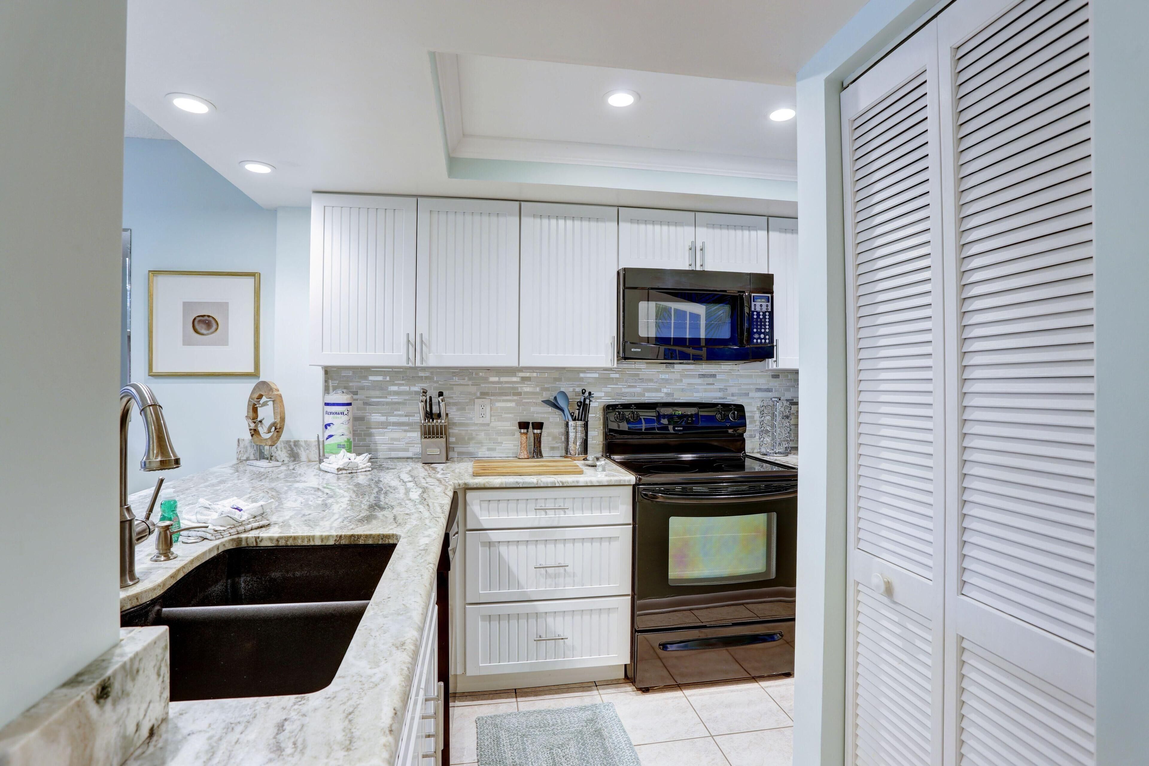 A kitchen with white cabinets, a black microwave, a stove, and a sink.