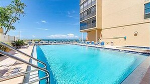 A swimming pool with a clear blue water surface, surrounded by a tiled deck and a building with a beige facade.