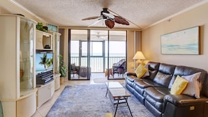 A living room with a leather sofa, a glass cabinet, a ceiling fan, and a view of the outdoors through a sliding door.