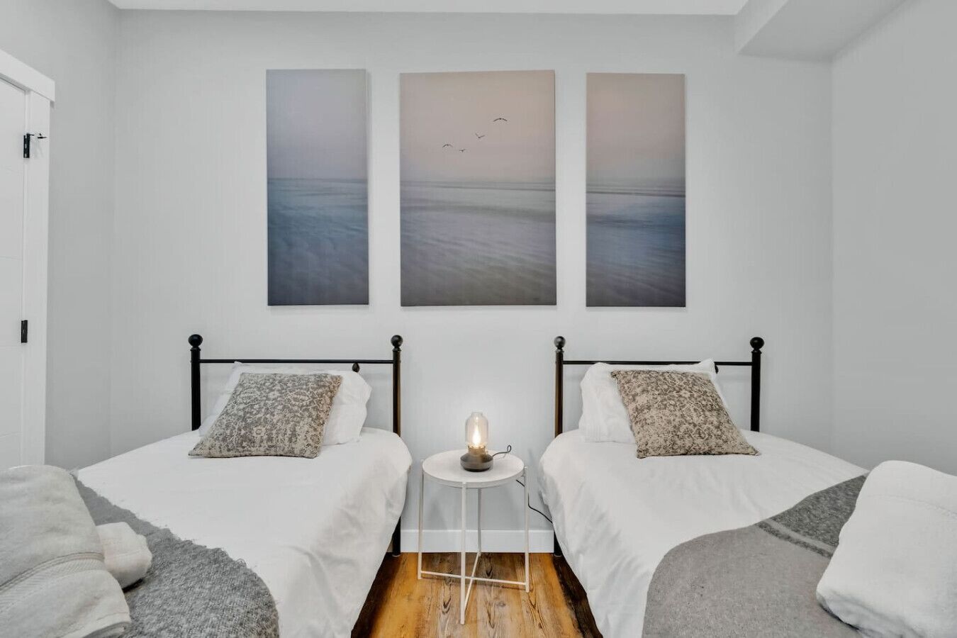 Ein Schlafzimmer mit zwei Betten, einem Nachttisch mit Lampe und drei großen Wandbildern mit Meerlandschaften.
