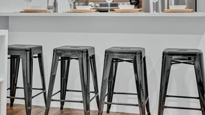 Une cuisine moderne avec un plan de travail blanc, quatre tabourets noirs et des verres à vin.