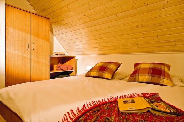 Un dormitorio con techo de madera, una cama con almohadones a cuadros, una mesita de noche y un armario.