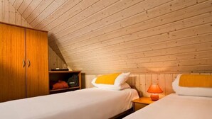 A room with two beds, wooden wardrobe, and a lamp.