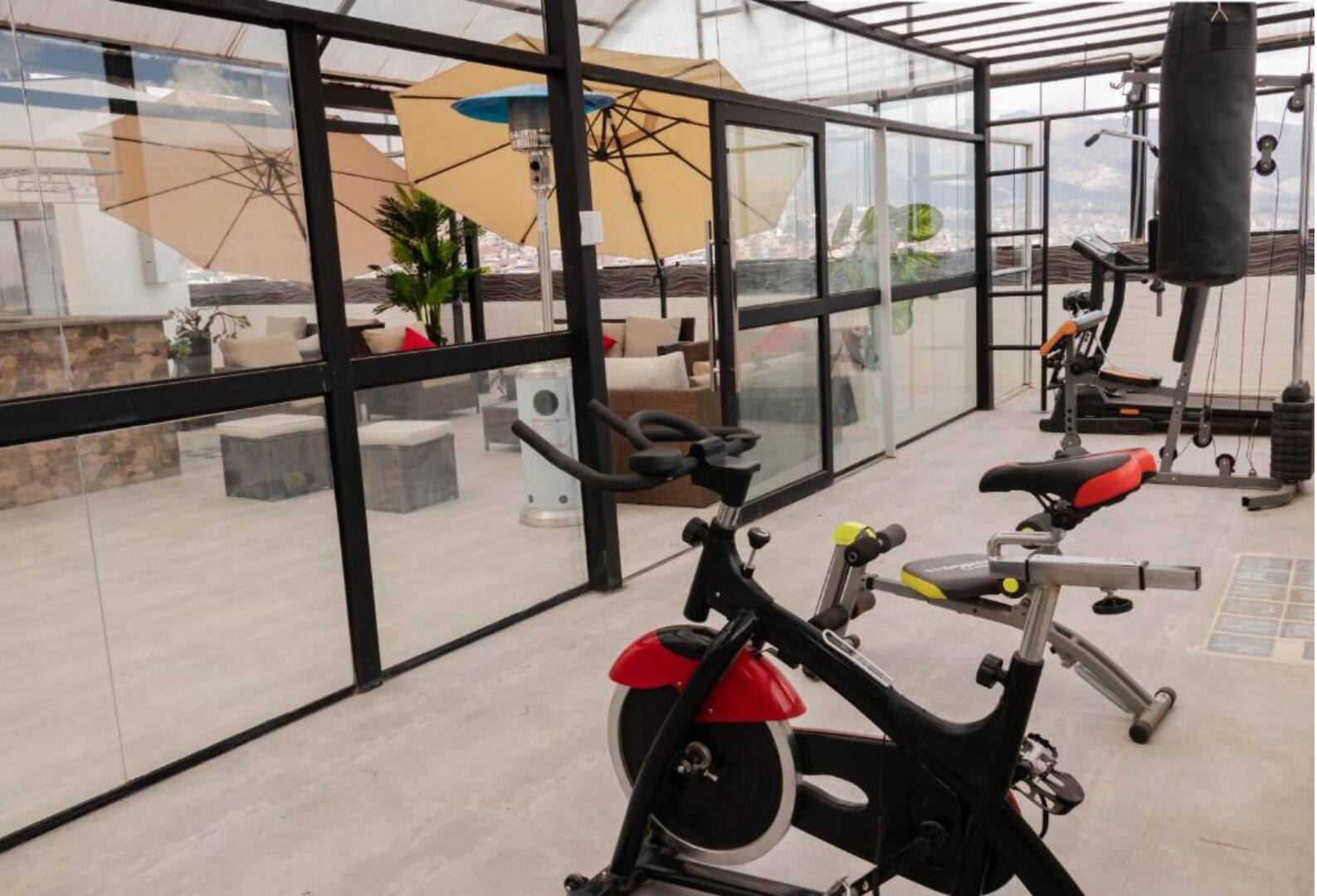 A gym with exercise bikes and a punching bag, large windows, and outdoor seating.