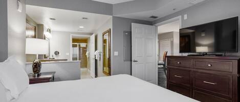 Une chambre d’hôtel avec un grand lit, une télévision, une commode et une salle de bain visible à travers une porte ouverte.
