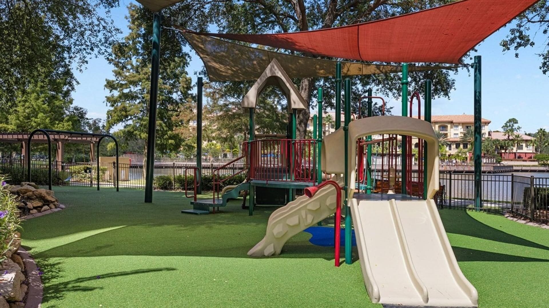 Un parque infantil con toboganes y estructuras para escalar, rodeado por una valla y vegetación.