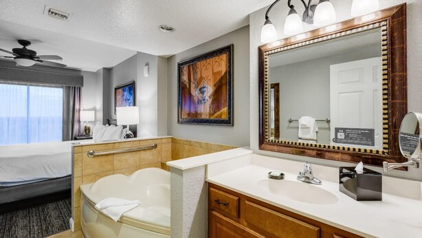 A hotel bathroom with a bathtub, a large mirror, a vanity with a sink, and a shower area.