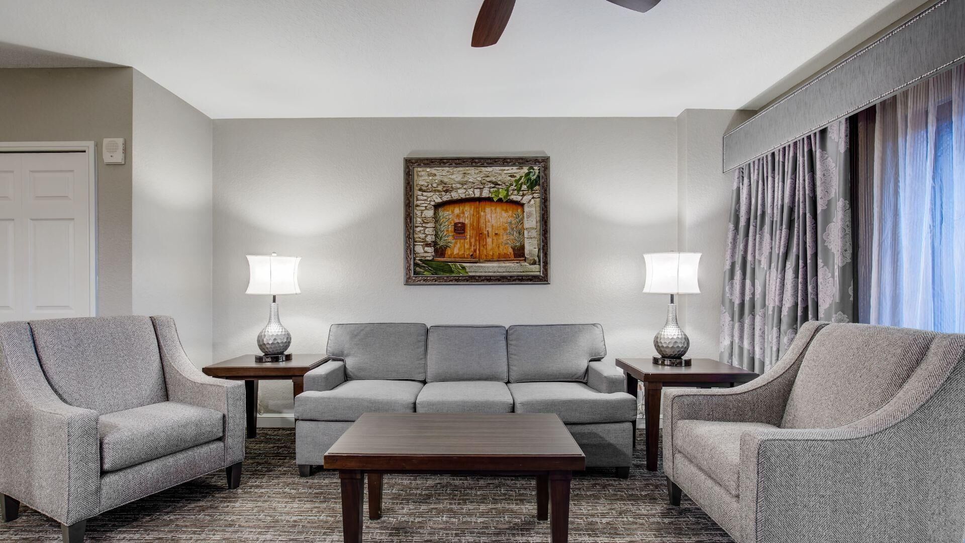 A living room with a grey sofa set, two side tables with lamps, a wooden coffee table, and a painting of a wooden door on the wall.
