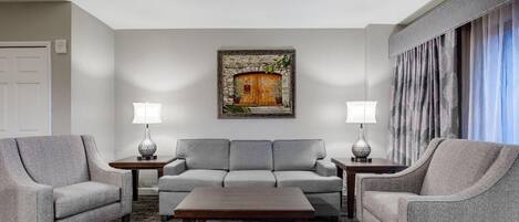 A living room with a grey sofa set, two side tables with lamps, a wooden coffee table, and a painting of a wooden door on the wall.
