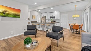 Un salon moderne avec une table basse en bois, deux fauteuils gris et un coin repas comprenant une table et des chaises.