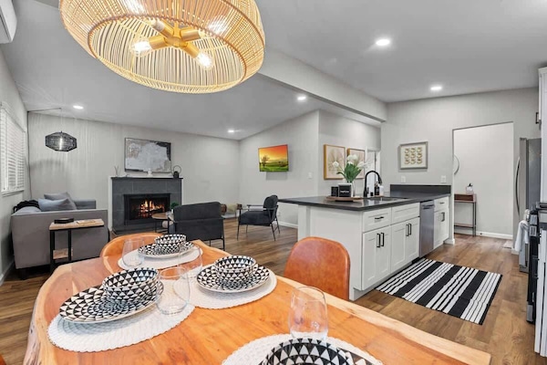 This open-concept space features a cozy living area with a fireplace, a stylish kitchen with an island, and a warm dining setup. Modern lighting, wood floors, and elegant decor create a welcoming atmosphere.