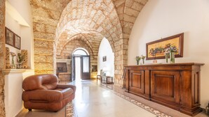 A spacious lobby with a stone archway, a leather armchair, a wooden reception desk, and a framed painting on the wall. - Palazzo Lily - Racale (Racale)