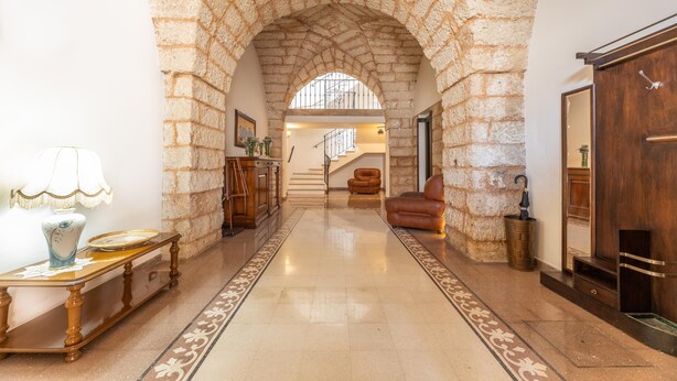 A stone archway leading to a staircase, a wooden bench, a leather armchair, and a wooden cabinet. - Palazzo Lily - Racale (Racale)