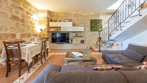 A cozy living room with a stone wall, a dining area with a table set for two, and a staircase with a railing. - Palazzo Lily - Racale (Racale)