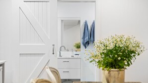 A bathroom with a white door, a sink, a mirror, and a towel rack. - Pipis Pretty Point - Couples Retreat (Malua Bay)
