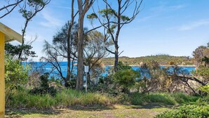 A coastal landscape with trees, a clear sky, and a view of the sea. - Pipis Pretty Point - Couples Retreat (Malua Bay)