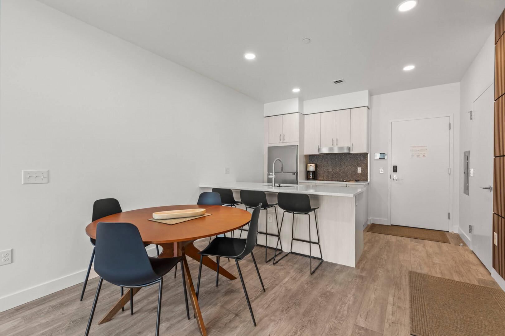 Une cuisine moderne avec des meubles blancs, un îlot central et un coin repas comprenant une table en bois et des chaises noires.