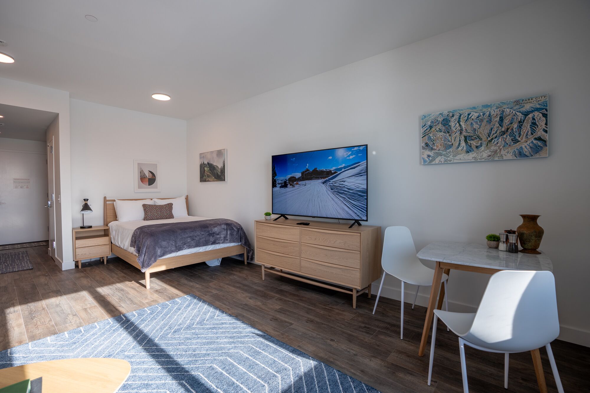 Un dormitorio moderno con cama, mesita de noche, cómoda, televisor y escritorio con sillas.