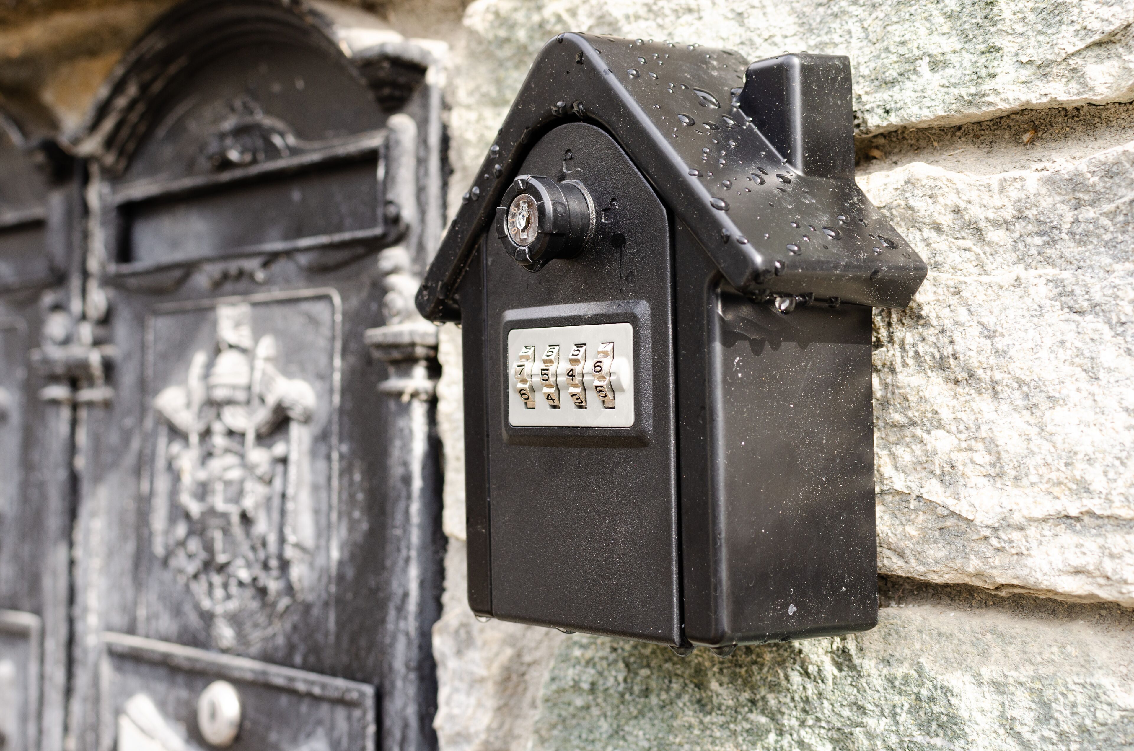A black metal mailbox with a keypad, mounted on a stone wall.
