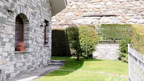 A stone building with a stone roof, a small garden with a hedge and a tree, and a metal fence. - Sarre Skyline Apartment - Relaxation in Aosta Valley (Montan-angelin-arensod)