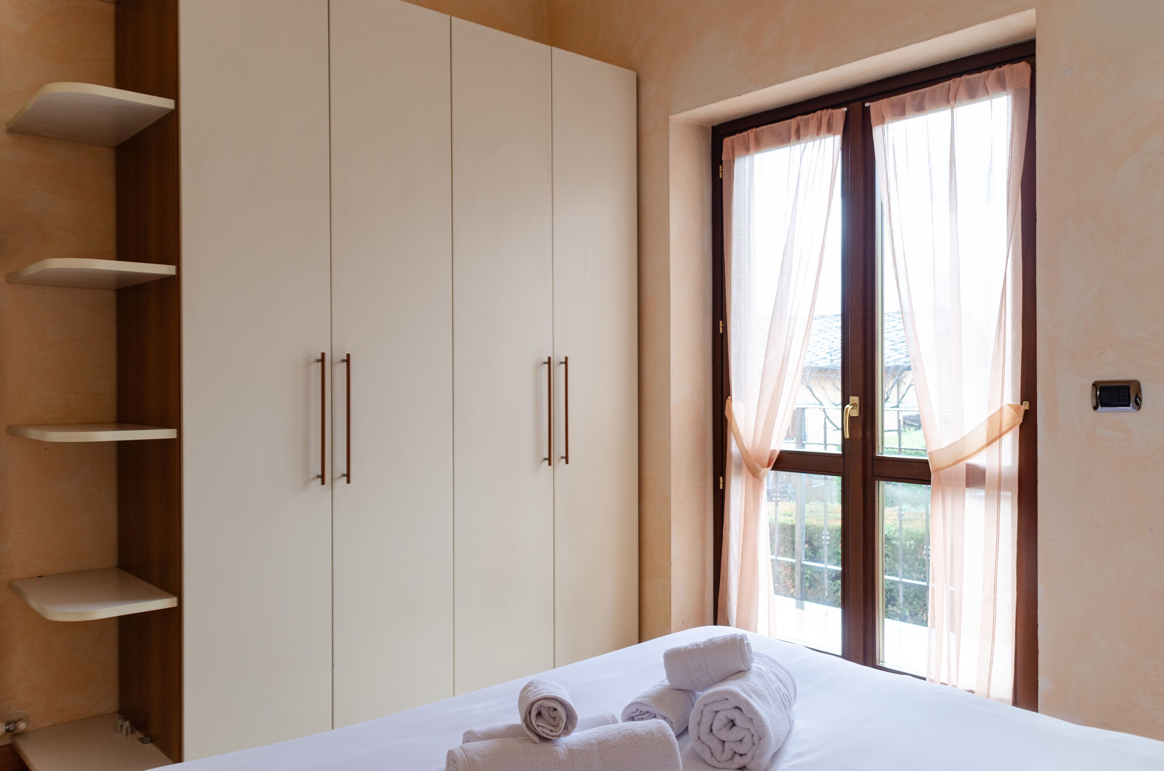 Une chambre à coucher avec un lit, une armoire blanche et une fenêtre avec des rideaux.