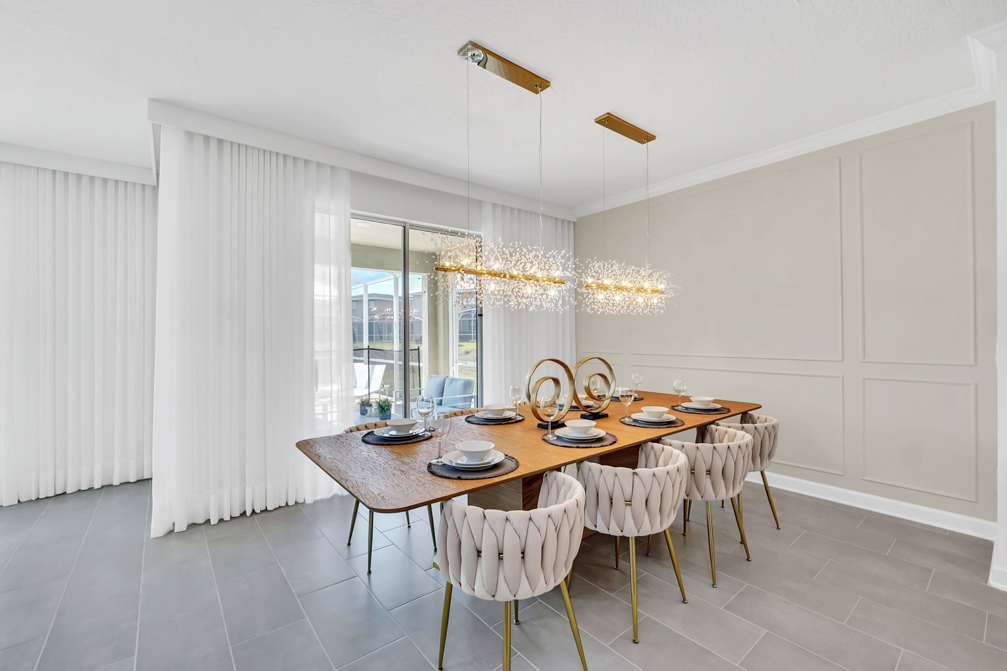 A modern dining room with a wooden table, white upholstered chairs, and a chandelier.