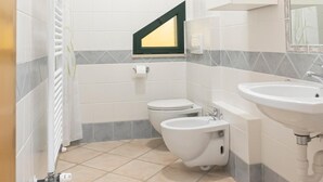 Un baño con inodoro, bidé y lavamanos, paredes con azulejos y una ventana.