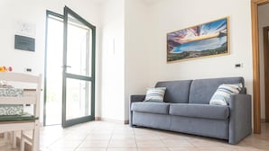 Un salón con un sofá gris, una silla blanca, un ventanal grande y un cuadro en la pared.